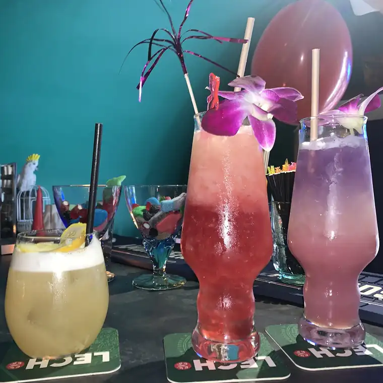 Trzy kolorowe drinki z orchideami na tle turkusowej ściany