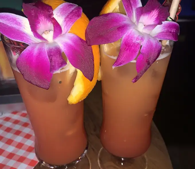 Dwa pomarańczowe drinki z fioletowymi orchideami